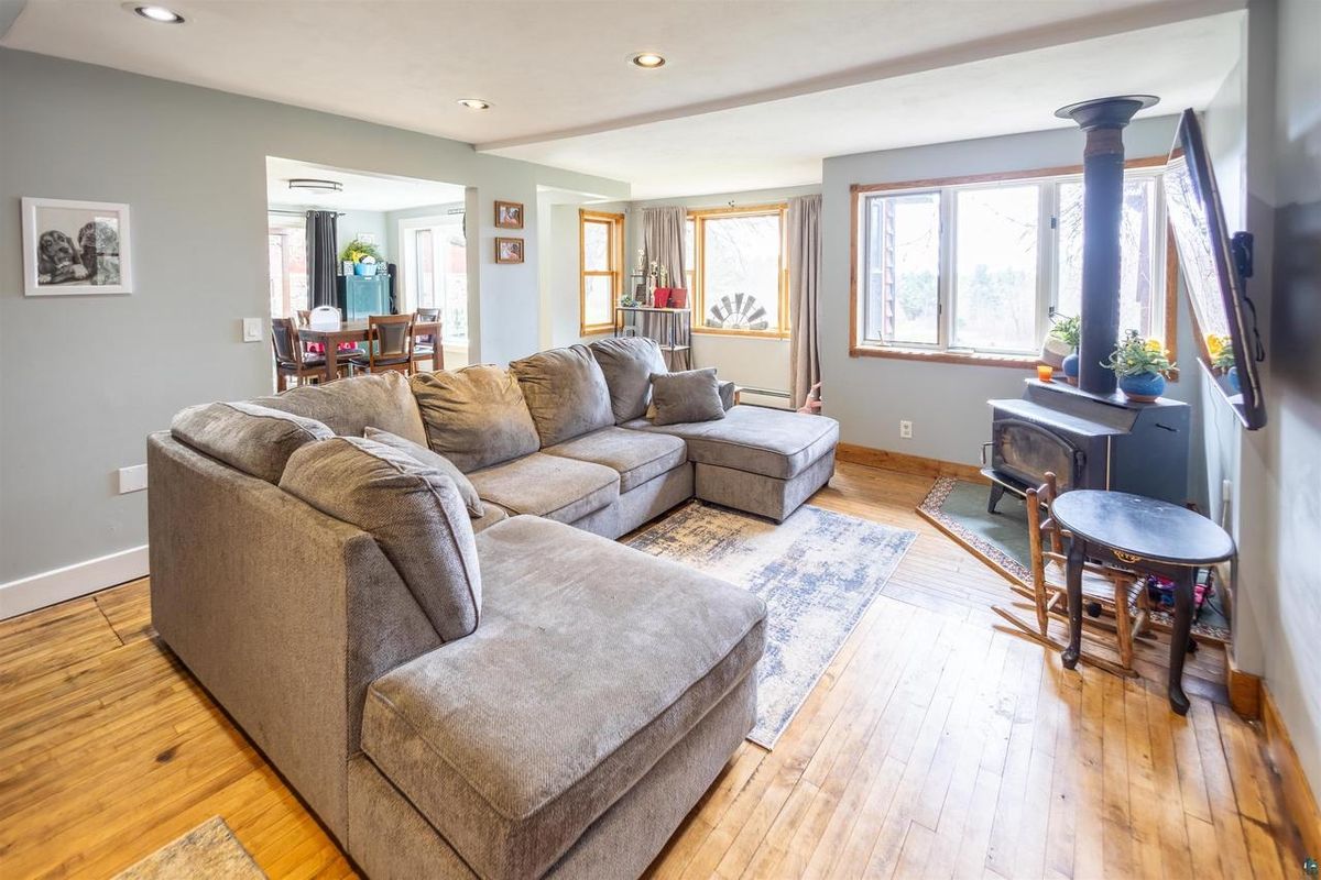 Living room with a sectional sofa, a wood stove, and wide-plank wood floors.